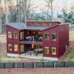 Sunset Lodge Sets modern red cabin with rooftop deck and large windows in a wooded setting