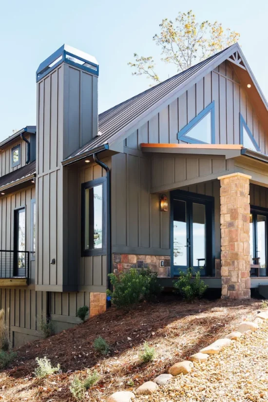 Modern dark gray lodge exterior with a metal roof, stone columns, large windows, and a landscaped entrance.